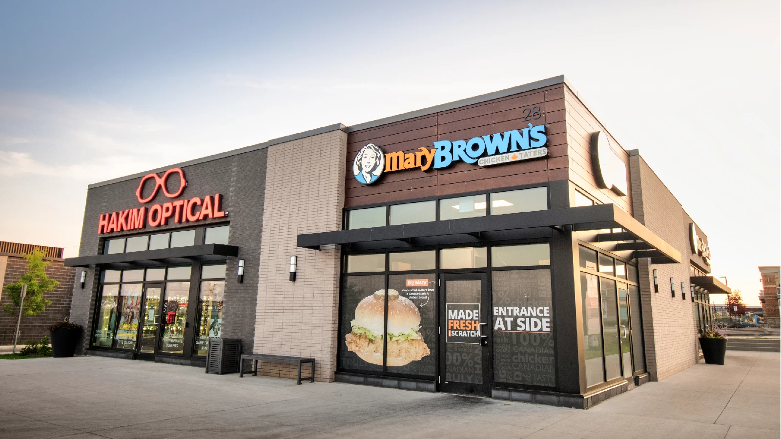 Clair Marketplace, Guelph – Hakim Optical and Mary Brown's storefronts at dusk