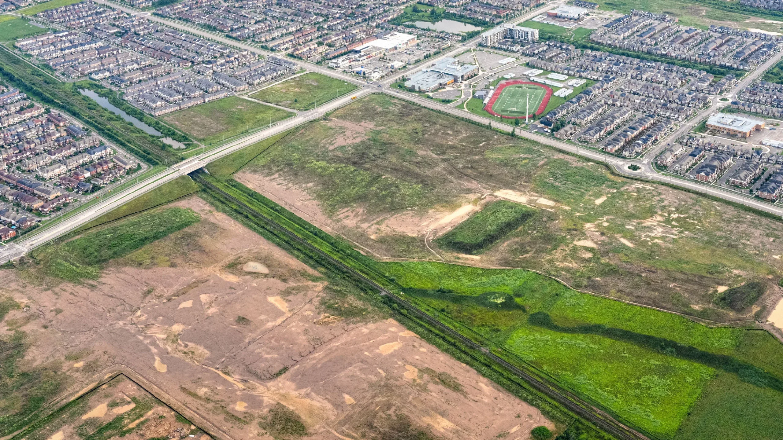 Bronte St S & Louis St. Laurent Ave (SWC), Milton – aerial view of the graded site beside a subdivision and road