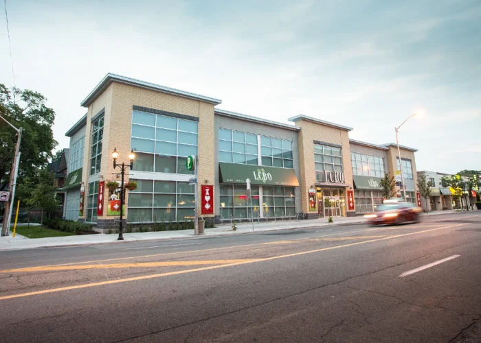 Danforth Ave & Ellerbeck St, Toronto – two-storey retail building with LCBO from across the street at dusk