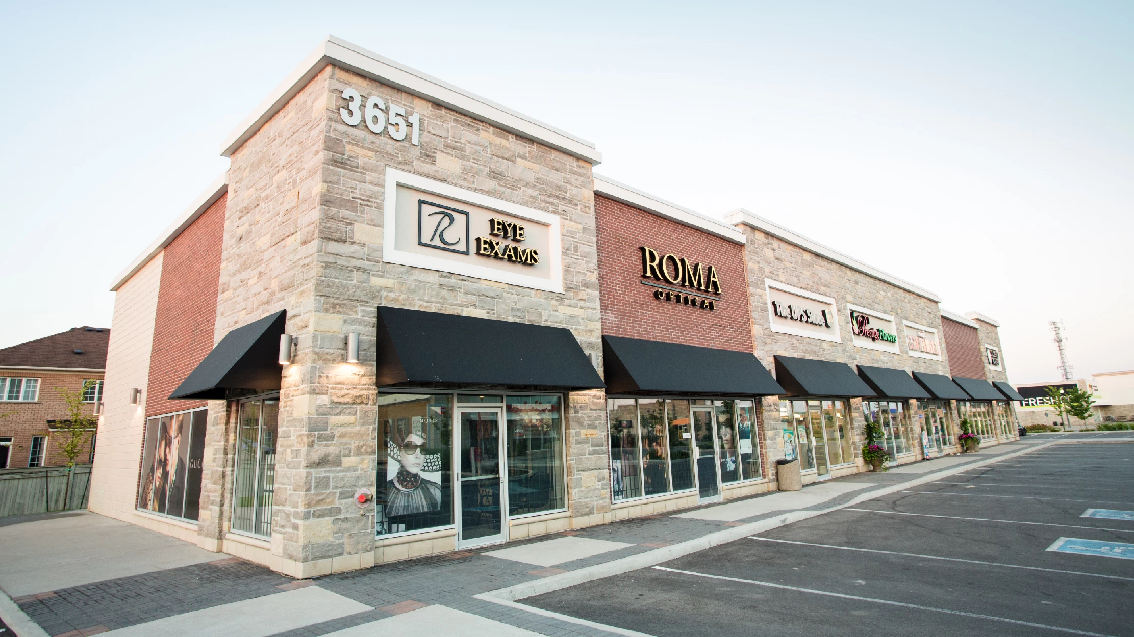 Vellore Village - Phase II, Vaughan – stone-clad retail row with black awnings and an optical shop