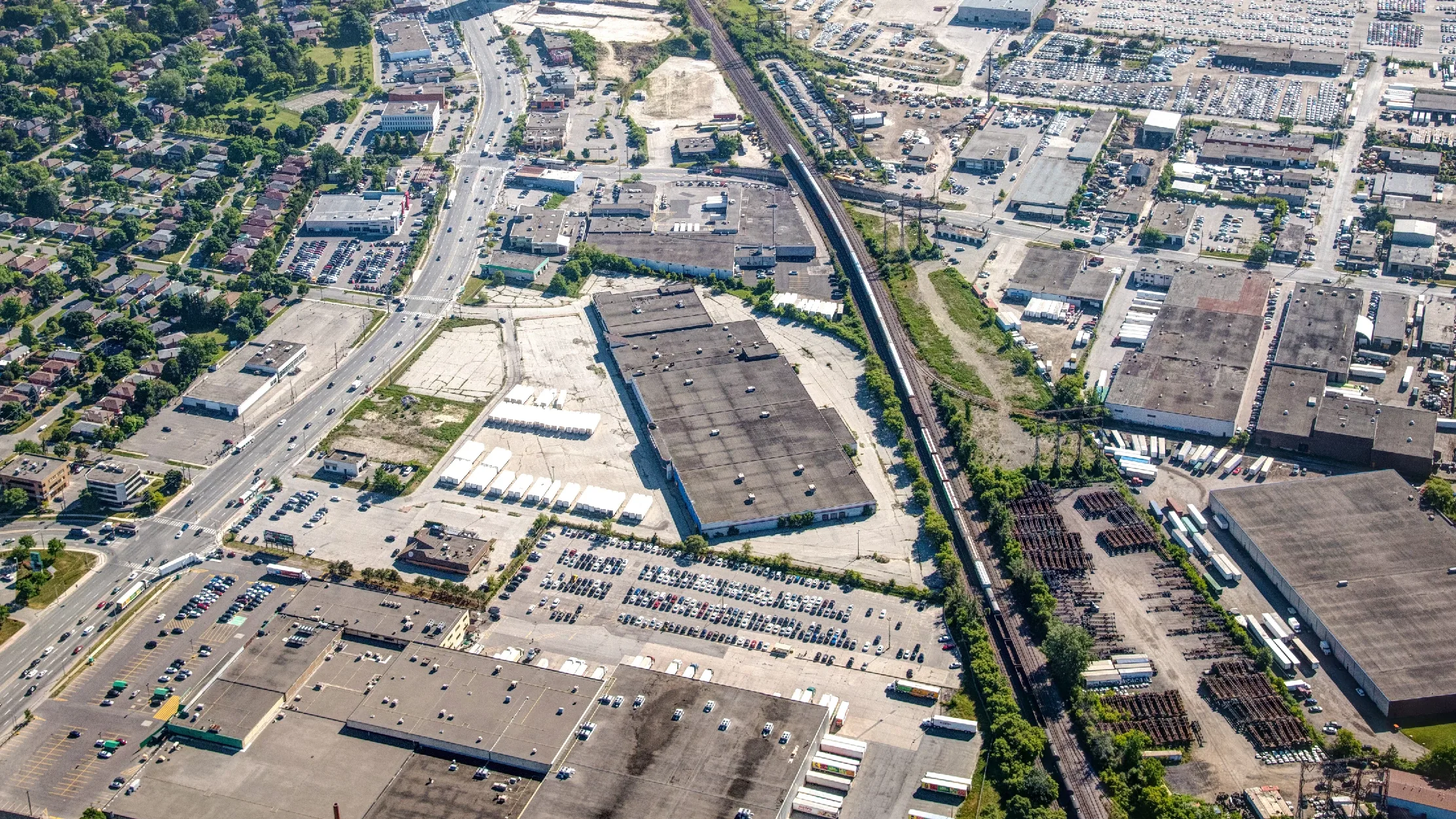 Honeydale Mall Redevelopment, Toronto – aerial view of the mall and parking lots beside a rail corridor