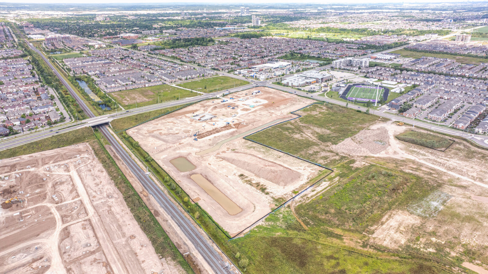 Bronte St S & Louis St. Laurent Ave (SWC), Milton – aerial view of the graded site beside a subdivision and sports field