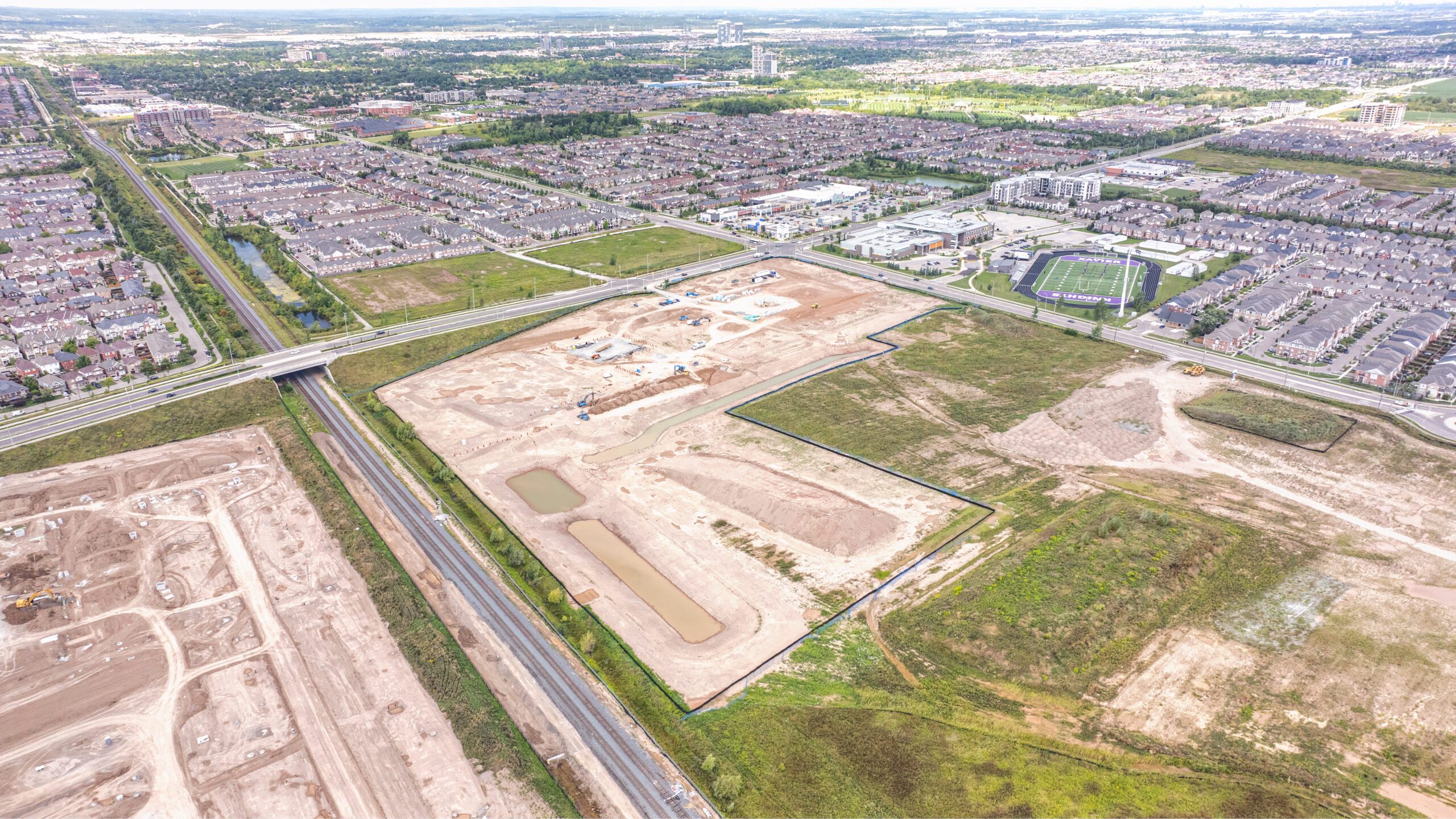 Bronte St S & Louis St. Laurent Ave (SWC), Milton – aerial view of the graded site beside a subdivision and sports field