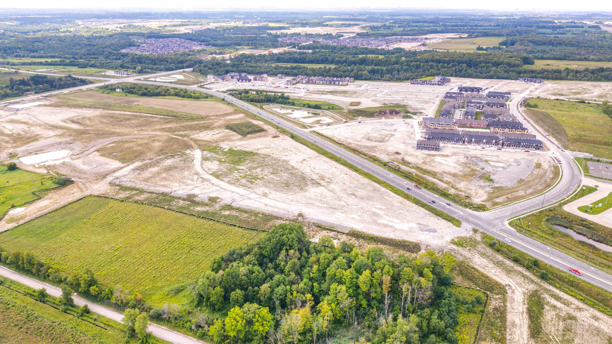 Brock Rd & 16 Sideroad, Pickering – aerial view of the graded site beside a road and woodlot